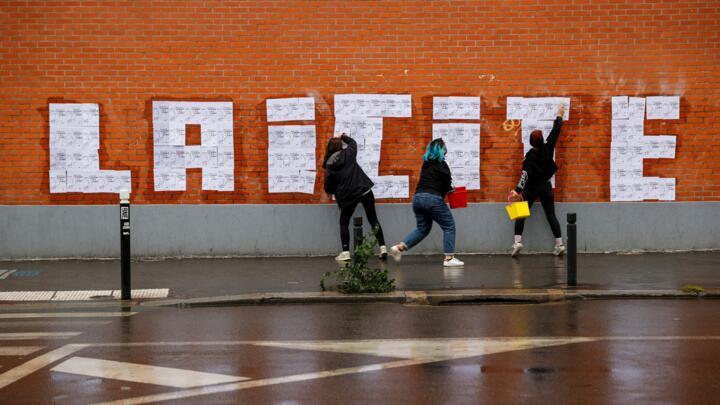 Three feminist activists placard posters of a drawing by French cartoonist Charb to read  " Laicite " in Montreuil, on October 20, 2020.