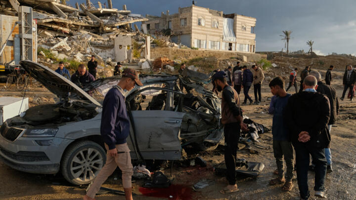 Palestinians looks at a destroyed car following an Israeli strike in Gaza City on December 13, 2025